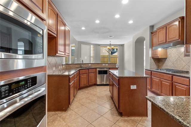 kitchen with stone counters, sink, an inviting chandelier, a kitchen island, and appliances with stainless steel finishes