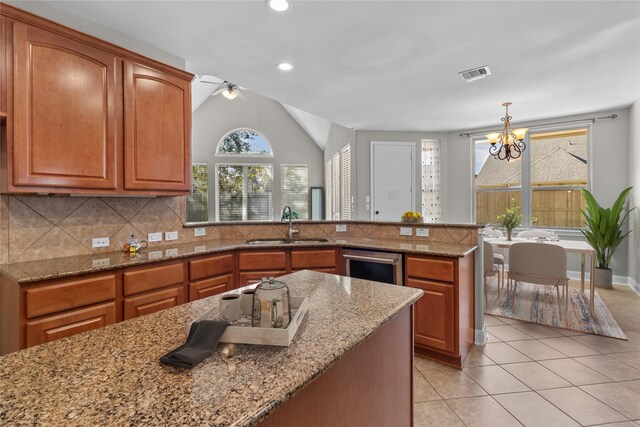 kitchen with light stone countertops, ceiling fan with notable chandelier, vaulted ceiling, sink, and pendant lighting