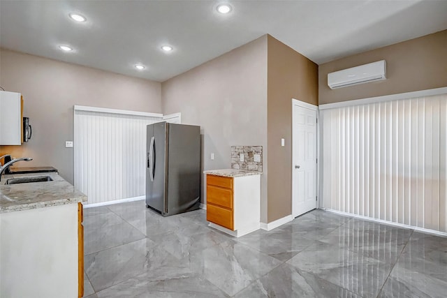 kitchen with a wall mounted AC, stainless steel fridge, sink, and light stone counters