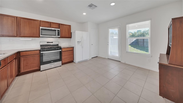 kitchen with light tile patterned floors, light stone countertops, appliances with stainless steel finishes, and tasteful backsplash