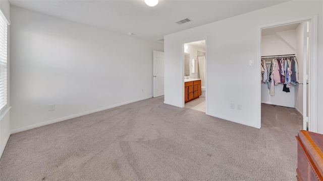 unfurnished bedroom with connected bathroom, light colored carpet, a spacious closet, and a closet