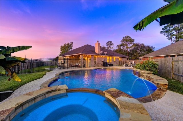 pool at dusk featuring an in ground hot tub and pool water feature