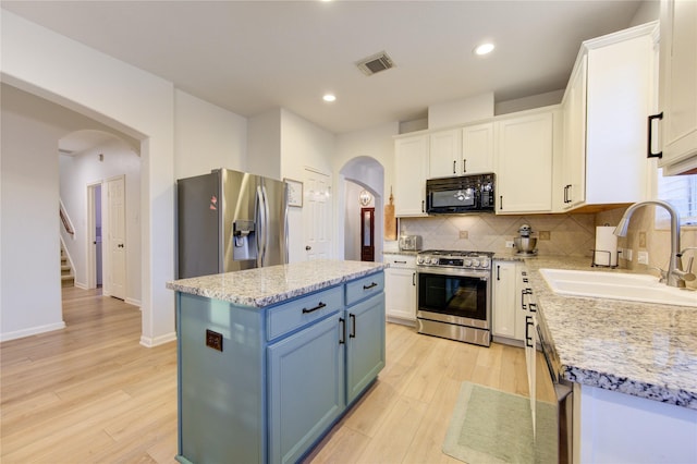 kitchen with stainless steel appliances, a kitchen island, white cabinetry, and sink