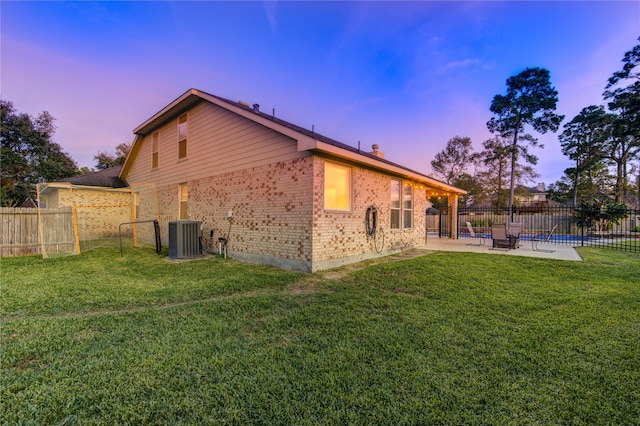 back house at dusk featuring a yard, a patio, and central AC unit