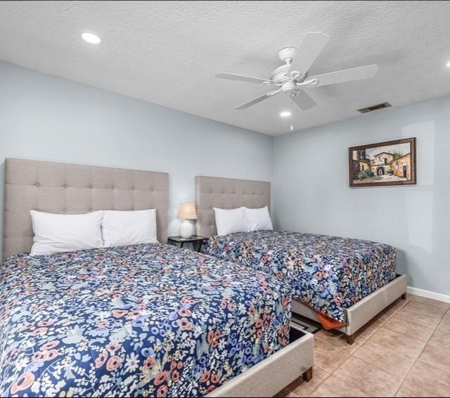 bedroom with ceiling fan, light tile patterned floors, and a textured ceiling