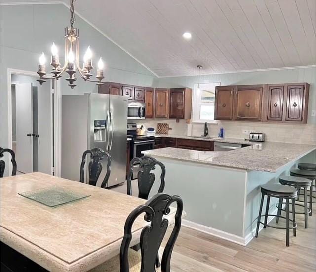 kitchen featuring pendant lighting, lofted ceiling, an inviting chandelier, light hardwood / wood-style flooring, and stainless steel appliances