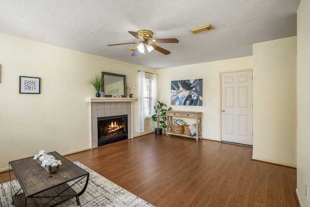 living room featuring a textured ceiling, ceiling fan, dark wood-type flooring, and a tile fireplace