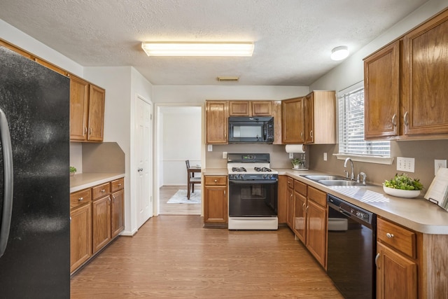 kitchen featuring a textured ceiling, sink, light hardwood / wood-style floors, and black appliances