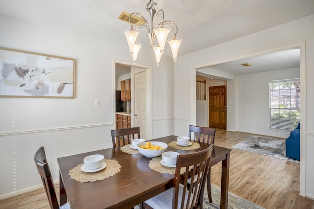 dining area featuring a textured ceiling, light wood-type flooring, and an inviting chandelier