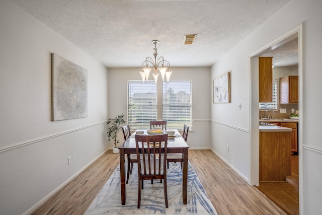 dining space featuring sink, light wood-type flooring, a textured ceiling, and a chandelier