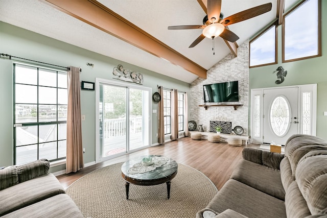 living room featuring high vaulted ceiling, a stone fireplace, ceiling fan, a textured ceiling, and light hardwood / wood-style floors