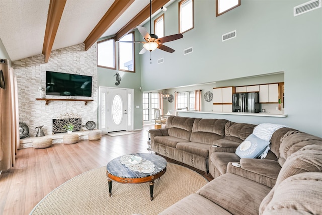 living room featuring high vaulted ceiling, a stone fireplace, ceiling fan, beam ceiling, and light hardwood / wood-style floors