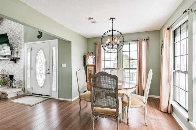 dining room with a fireplace, hardwood / wood-style flooring, a healthy amount of sunlight, and a notable chandelier