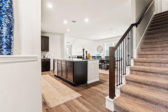 kitchen with sink, light wood-type flooring, dark brown cabinetry, and an island with sink