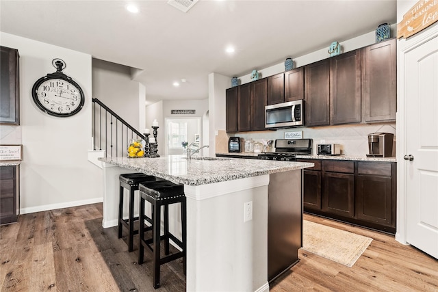 kitchen featuring black gas stove, a center island with sink, light hardwood / wood-style flooring, and a kitchen breakfast bar