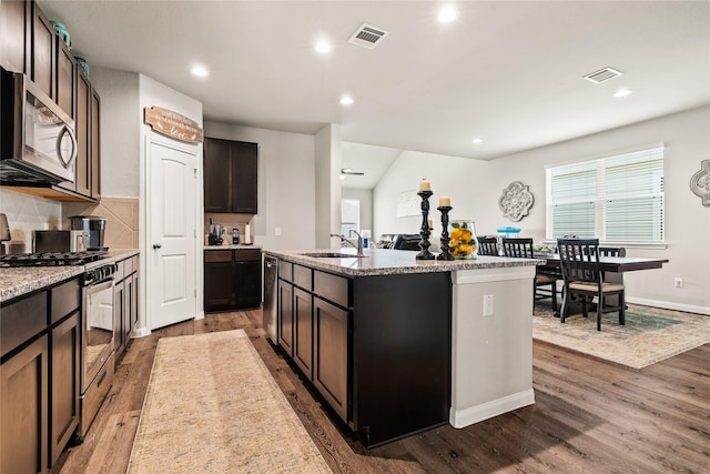 kitchen with dark brown cabinetry, sink, wood-type flooring, a center island with sink, and appliances with stainless steel finishes