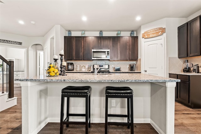 kitchen featuring hardwood / wood-style floors, dark brown cabinets, a kitchen island with sink, and a breakfast bar area