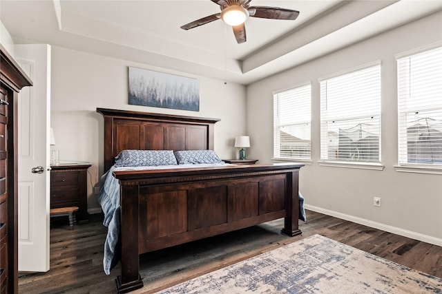 bedroom featuring dark hardwood / wood-style flooring, a tray ceiling, and ceiling fan