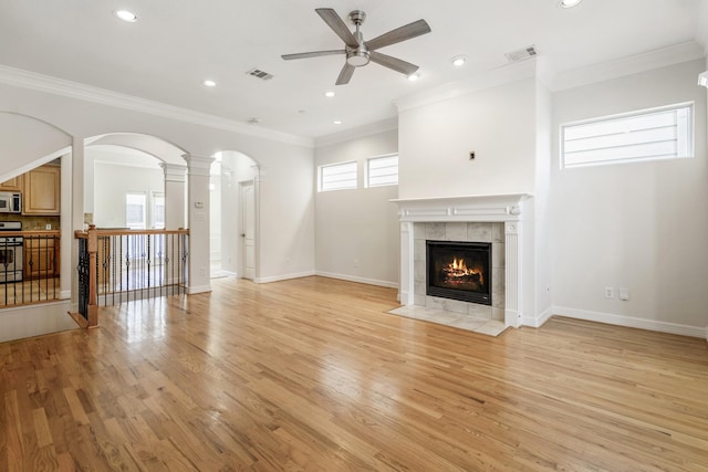 unfurnished living room with ornamental molding, a tile fireplace, ceiling fan, and light wood-type flooring