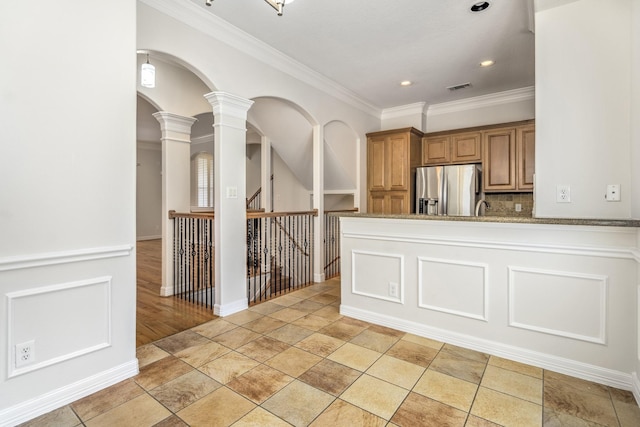 kitchen featuring crown molding, light stone counters, stainless steel fridge with ice dispenser, decorative columns, and backsplash