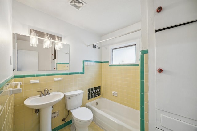 full bathroom with sink, tiled shower / bath combo, toilet, and tile walls