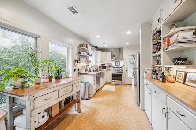 kitchen with white cabinets, appliances with stainless steel finishes, and wall chimney range hood