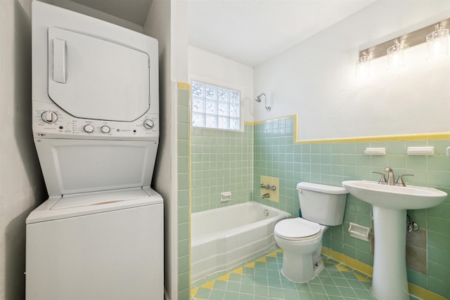 full bathroom with stacked washing maching and dryer, tile patterned floors, toilet, tile walls, and tiled shower / bath