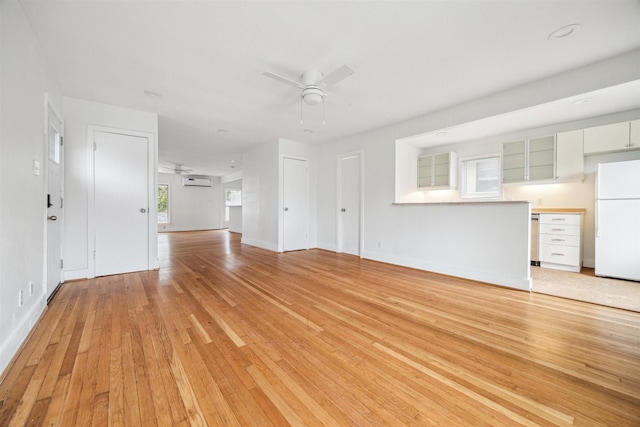 unfurnished living room with ceiling fan, light hardwood / wood-style flooring, and a wall mounted air conditioner