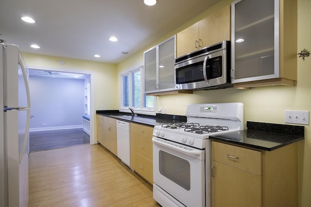 kitchen with white appliances, sink, light hardwood / wood-style flooring, dark stone countertops, and light brown cabinetry