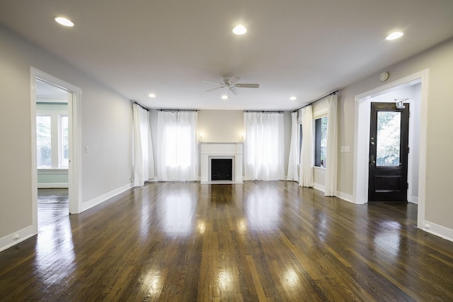 unfurnished living room featuring ceiling fan, a healthy amount of sunlight, and dark wood-type flooring