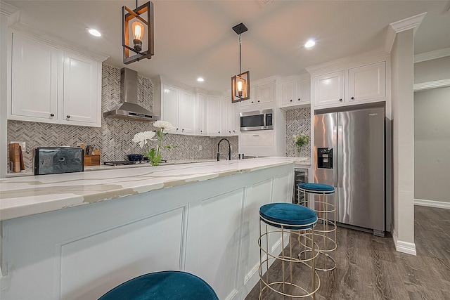 kitchen with appliances with stainless steel finishes, dark hardwood / wood-style flooring, wall chimney range hood, pendant lighting, and white cabinets