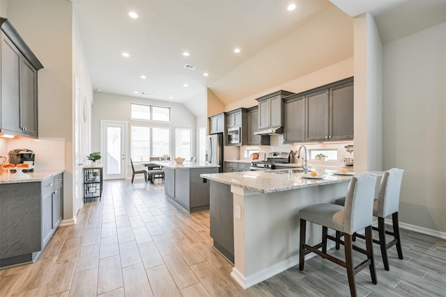 kitchen featuring sink, a center island, light stone counters, vaulted ceiling, and appliances with stainless steel finishes