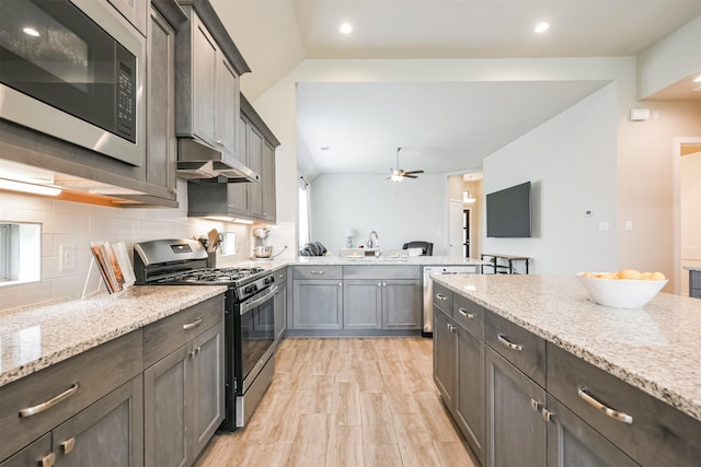 kitchen featuring light stone counters, ceiling fan, vaulted ceiling, and appliances with stainless steel finishes