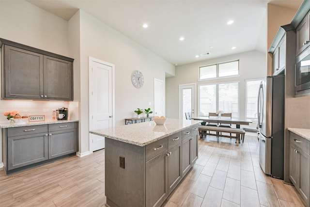 kitchen featuring a center island, decorative backsplash, light stone countertops, appliances with stainless steel finishes, and light hardwood / wood-style floors