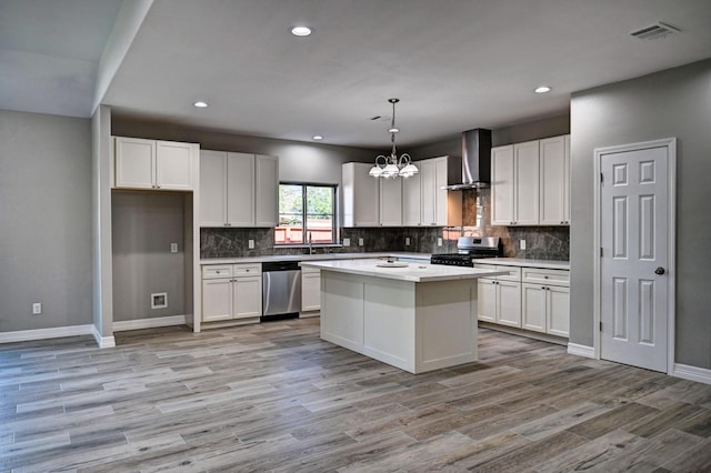 kitchen featuring white cabinets, hanging light fixtures, a center island, stainless steel appliances, and wall chimney range hood