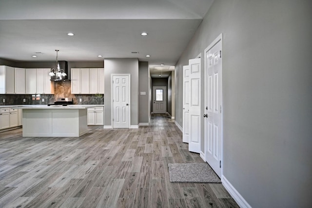 kitchen featuring pendant lighting, wall chimney range hood, a kitchen island, white cabinets, and stainless steel range oven