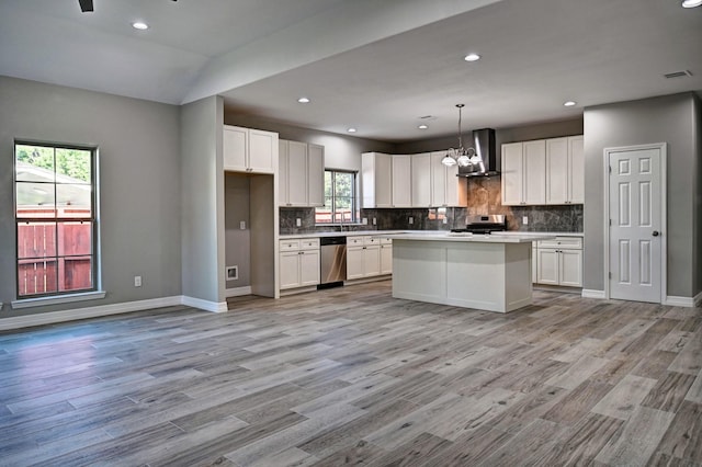 kitchen with appliances with stainless steel finishes, a kitchen island, decorative light fixtures, white cabinetry, and wall chimney exhaust hood