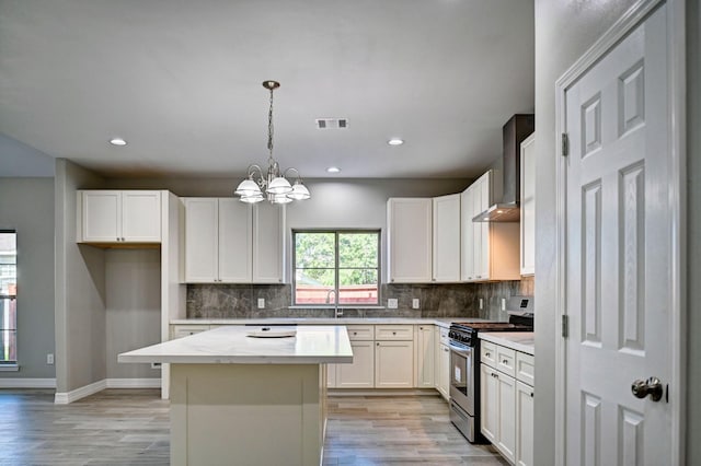 kitchen with hanging light fixtures, stainless steel range with gas stovetop, white cabinets, a kitchen island, and wall chimney exhaust hood