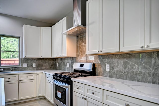 kitchen featuring wall chimney exhaust hood, tasteful backsplash, stainless steel range with gas cooktop, light stone countertops, and white cabinets