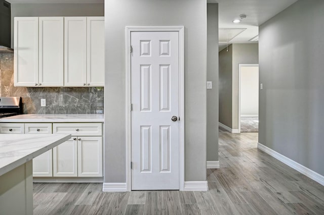 kitchen with white cabinetry, light stone counters, tasteful backsplash, stainless steel range, and light hardwood / wood-style floors