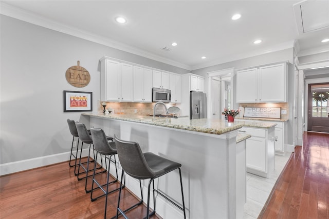 kitchen featuring kitchen peninsula, appliances with stainless steel finishes, light hardwood / wood-style floors, white cabinets, and ornamental molding