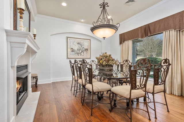 dining space with a tile fireplace, wood-type flooring, and ornamental molding