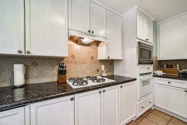 kitchen featuring backsplash, dark stone counters, white appliances, light tile patterned floors, and white cabinets