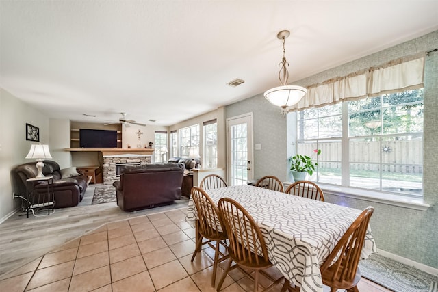 dining area featuring a stone fireplace, ceiling fan, plenty of natural light, and light hardwood / wood-style flooring