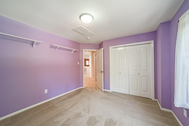 unfurnished bedroom with a textured ceiling, light carpet, and a closet