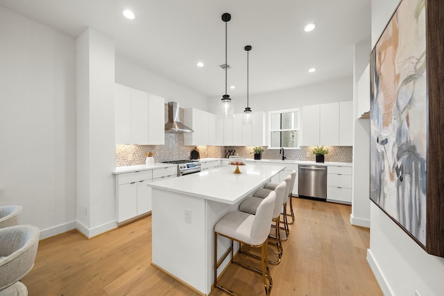 kitchen with white cabinetry, stainless steel appliances, a center island, decorative light fixtures, and wall chimney exhaust hood