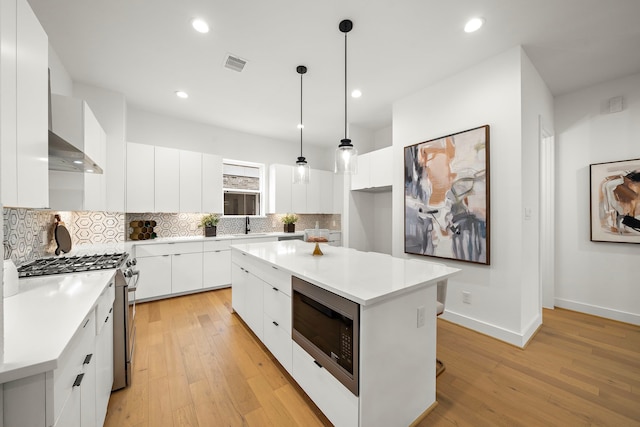 kitchen with built in microwave, decorative light fixtures, stainless steel stove, a kitchen island, and white cabinets