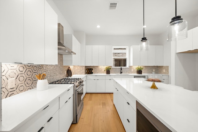 kitchen with sink, white cabinetry, hanging light fixtures, stainless steel appliances, and wall chimney range hood