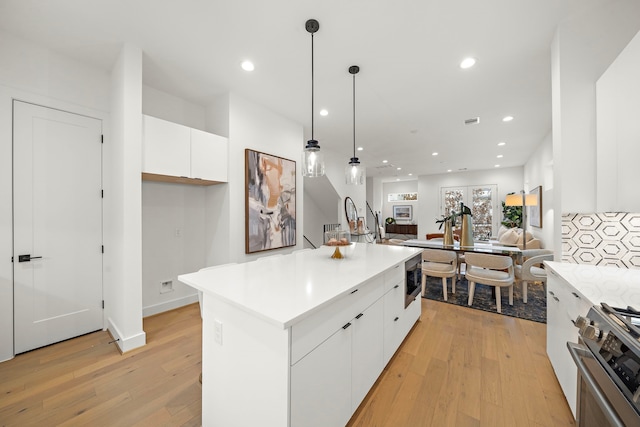 kitchen featuring pendant lighting, white cabinets, a center island, stainless steel appliances, and light hardwood / wood-style flooring