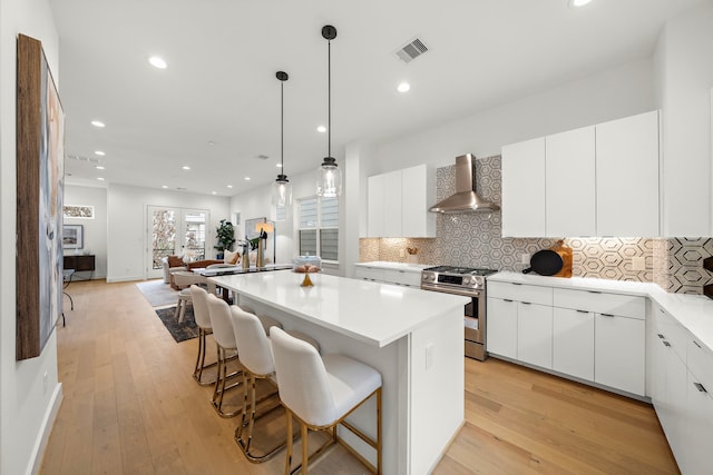 kitchen featuring gas range, white cabinetry, a breakfast bar, and wall chimney range hood